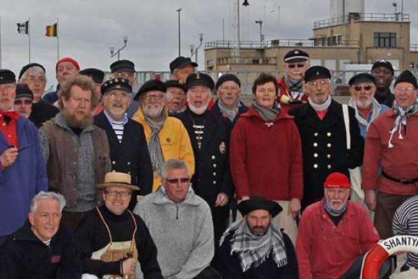 Foto van het Shantykoor van Blankenberg die gekleed zijn in traditionele klederdracht van de visserij en poseren met attributen typisch van de Vlaamse visserij. 